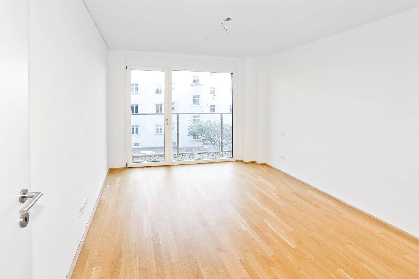 Helles, leeres Zimmer mit Parkettboden und Zugang zu einem französischen Balkon.