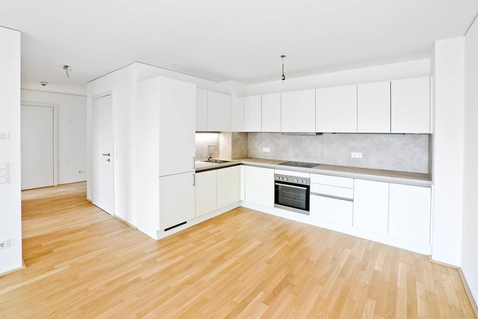 Moderne Einbauküche mit weißen Schränken, integrierten Geräten und Holzboden.