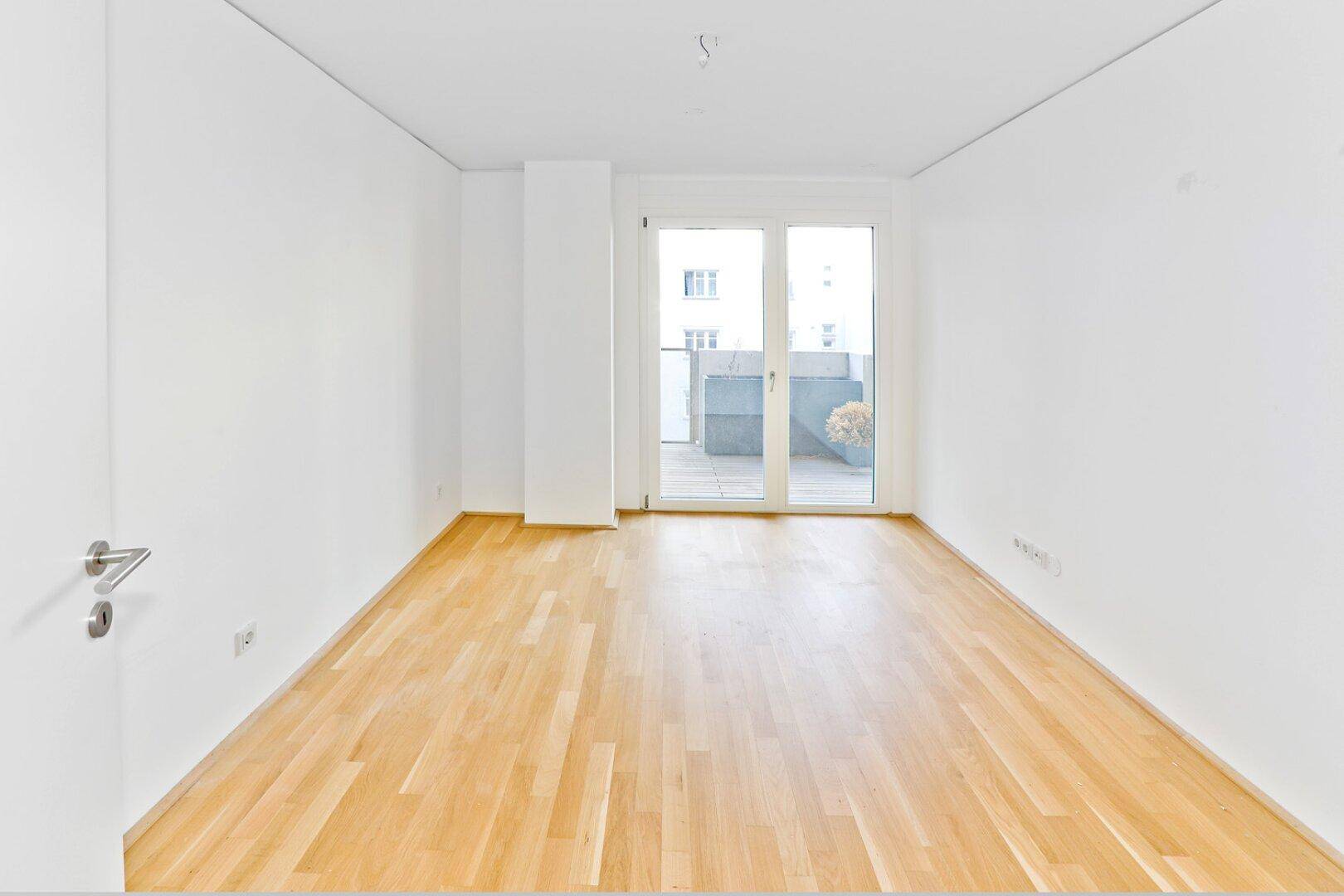 Geräumiges, helles Zimmer mit Holzboden und großen Fenstern, bereit zur Einrichtung.