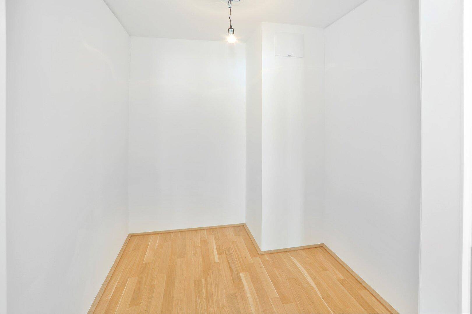 Kleiner, heller Raum mit Holzboden und weißen Wänden, ideal als Abstellraum.
