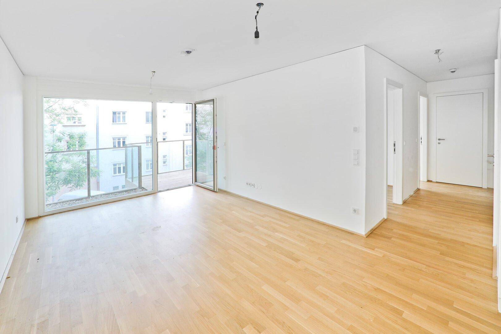 Großzügiger, heller Wohnbereich mit Parkettboden und Zugang zu einem Balkon.