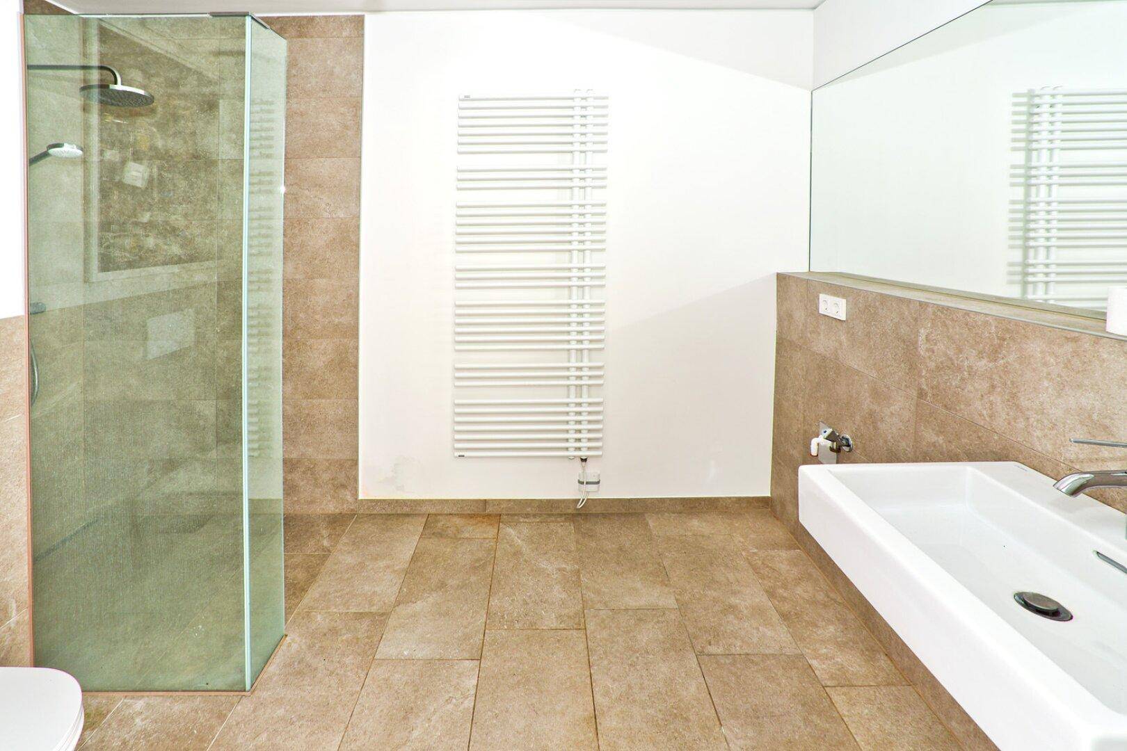 Modernes Badezimmer mit beigefarbenen Fliesen, ebenerdiger Dusche und beheiztem Handtuchhalter.