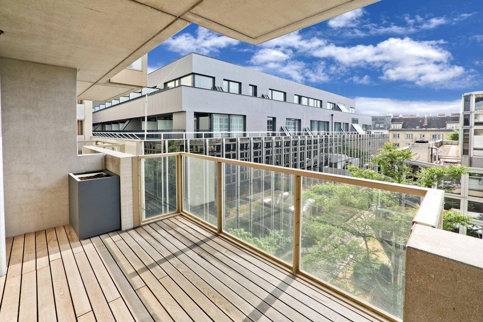Heller Balkon mit Holzdeck und Glasbrüstung, umgeben von zeitgenössischer Architektur.