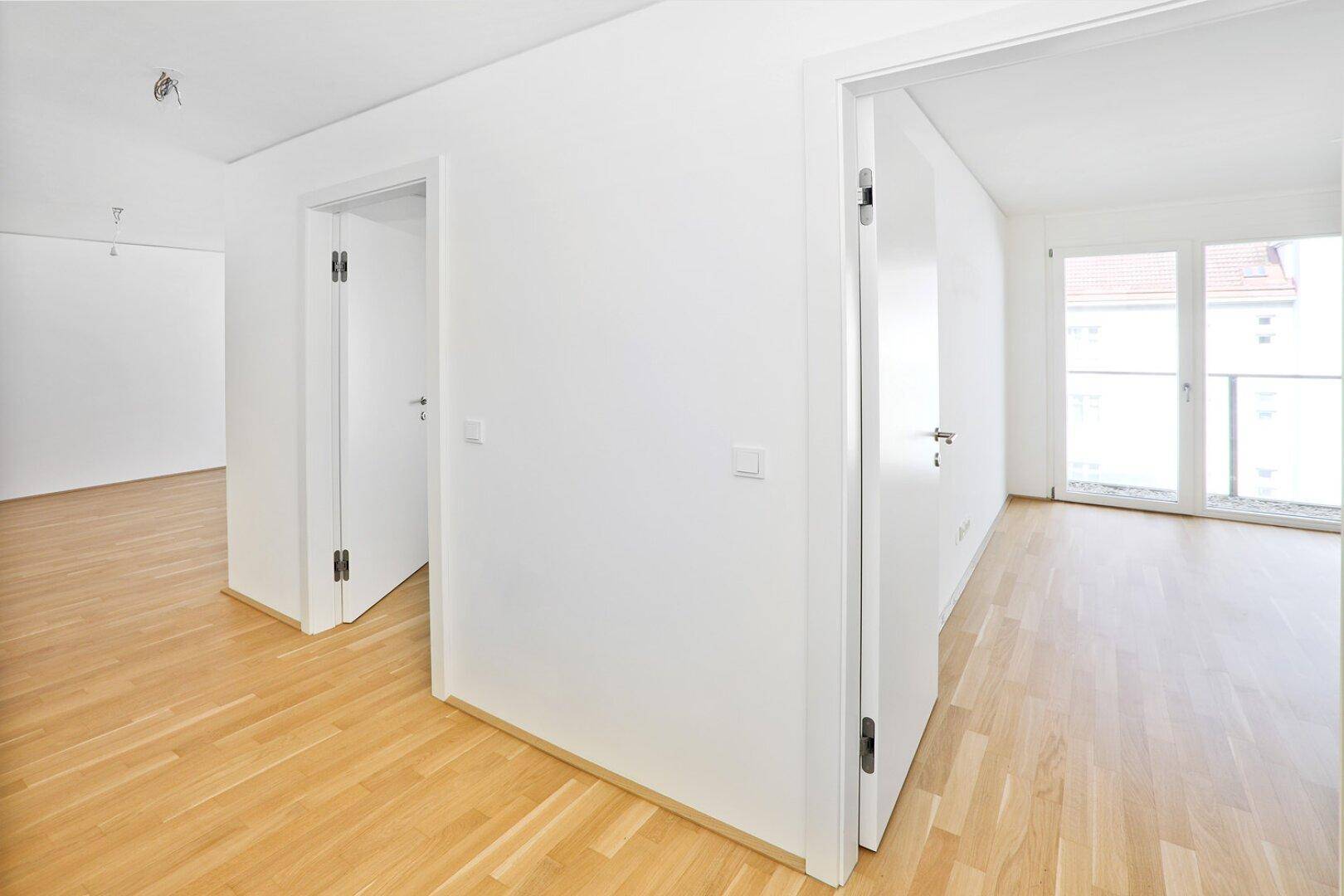 Heller Flur mit Parkettboden, der zu verschiedenen Zimmern und einem Balkon führt.