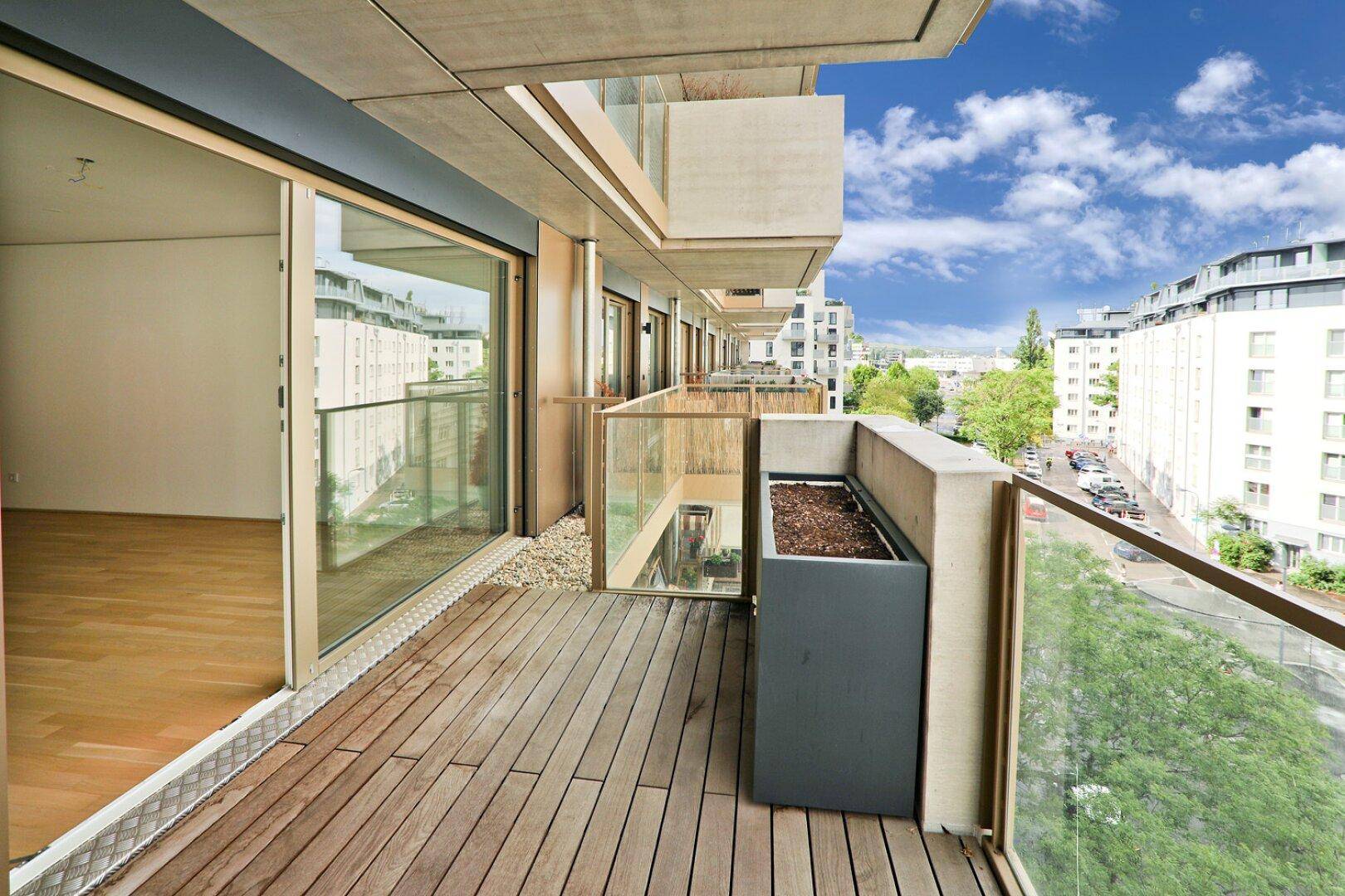 Geräumiger Balkon mit Holzboden und Glasgeländer, bietet einen weiten Blick über die Stadt.