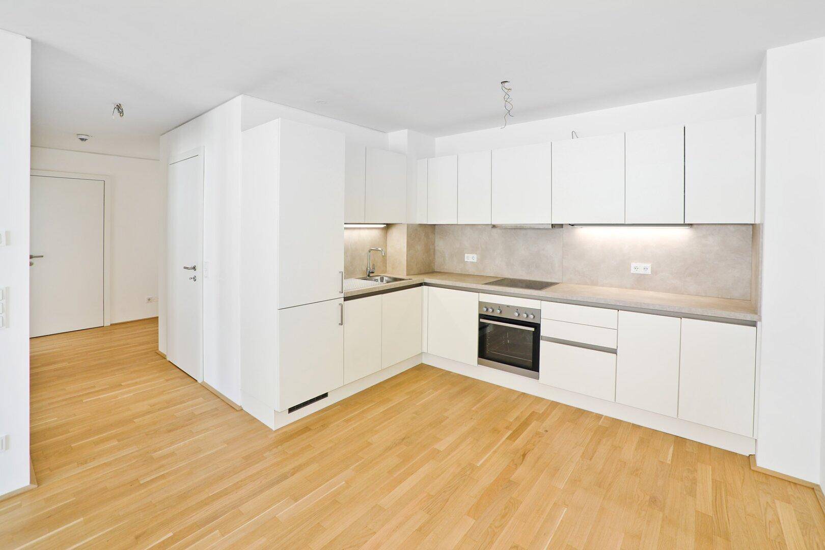 Moderne Einbauküche in Weiß mit integrierten Geräten und hellem Parkettboden.