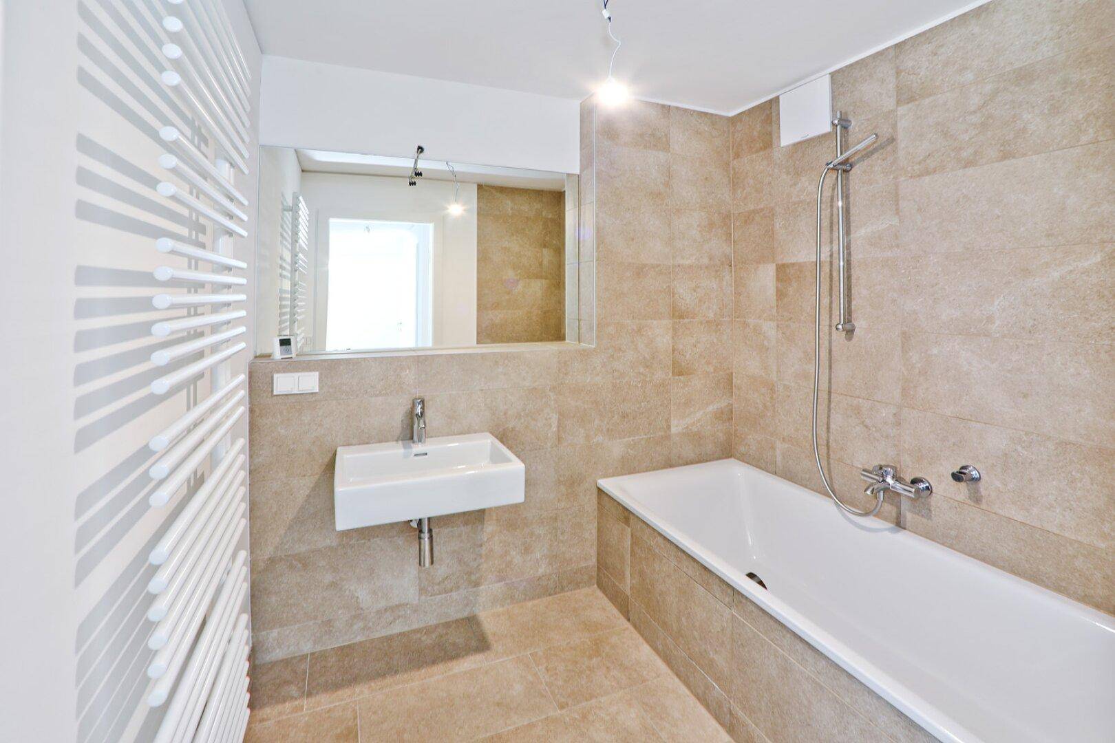 Modernes Badezimmer mit beigefarbenen Fliesen, Badewanne, Einzelwaschbecken und Handtuchheizkörper.