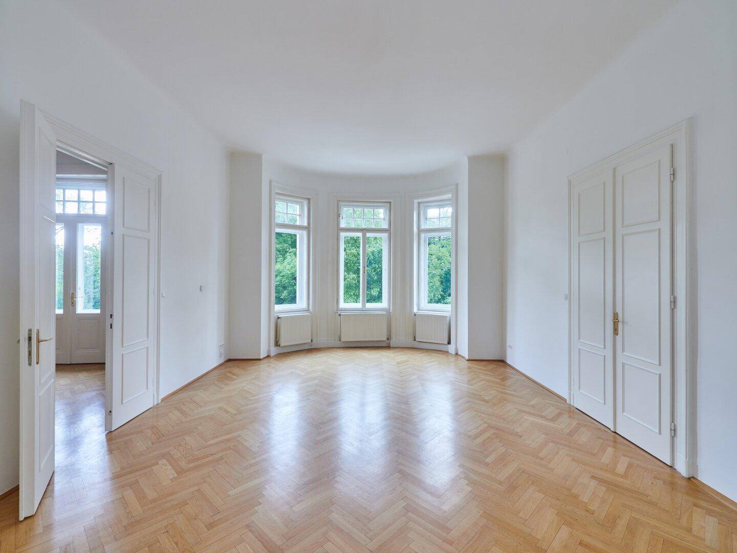 Geräumiges, helles Zimmer mit Fischgrätparkett und großen Erkerfenstern mit Blick ins Grüne.