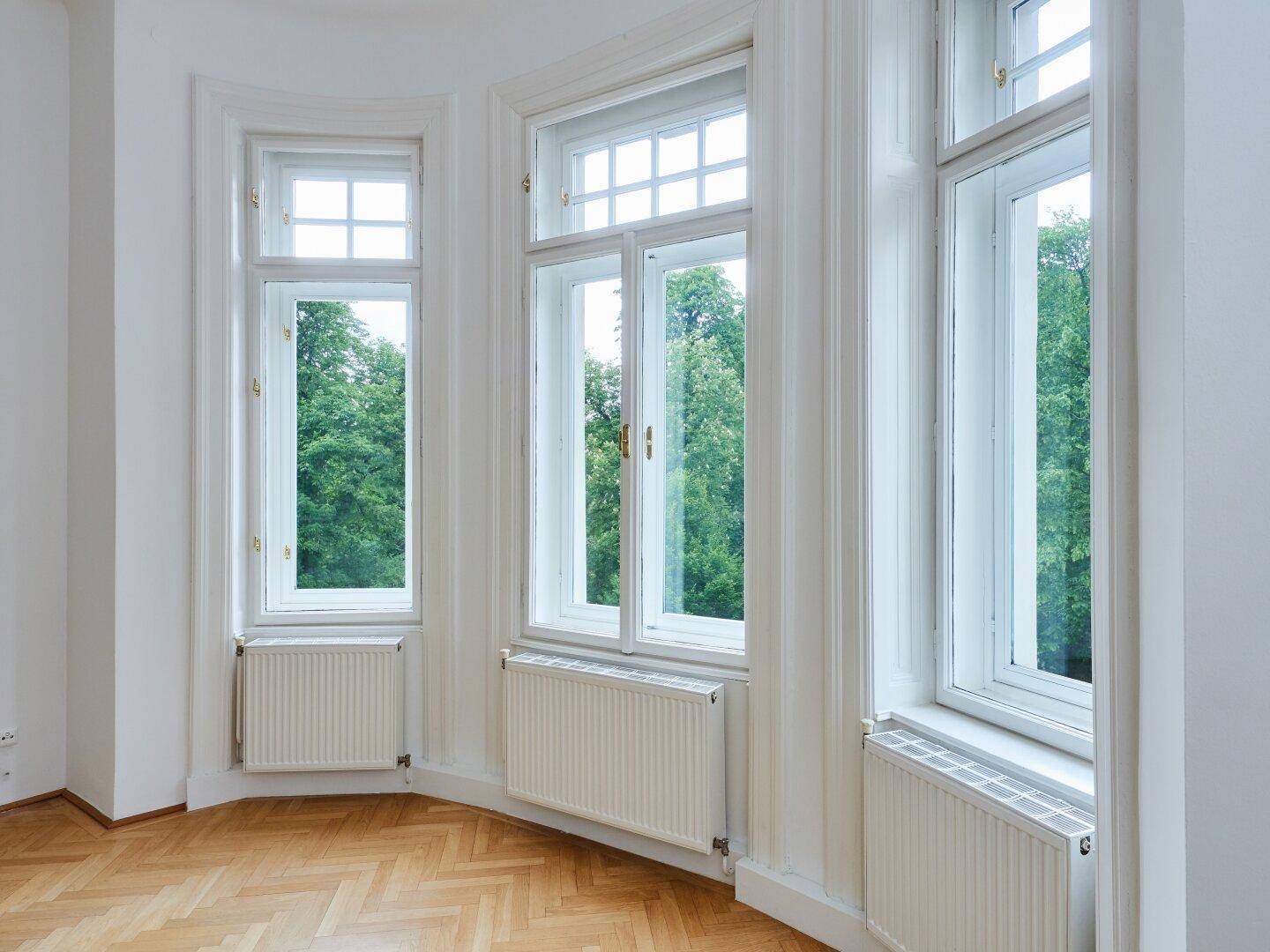 Detailansicht der hohen Erkerfenster mit Blick auf grüne Bäume und Heizkörper darunter.
