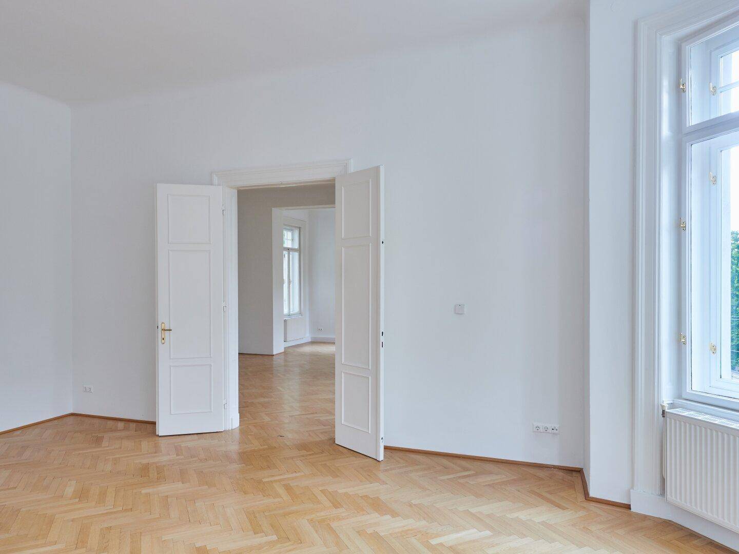 Helles Zimmer mit Fischgrätparkett und weißen Türen, die eine Verbindung zu anderen Räumen schaffen.