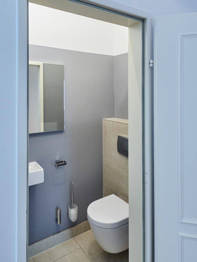 Kleines Gäste-WC mit modernem Wand-WC, Waschbecken und grauen Wänden.