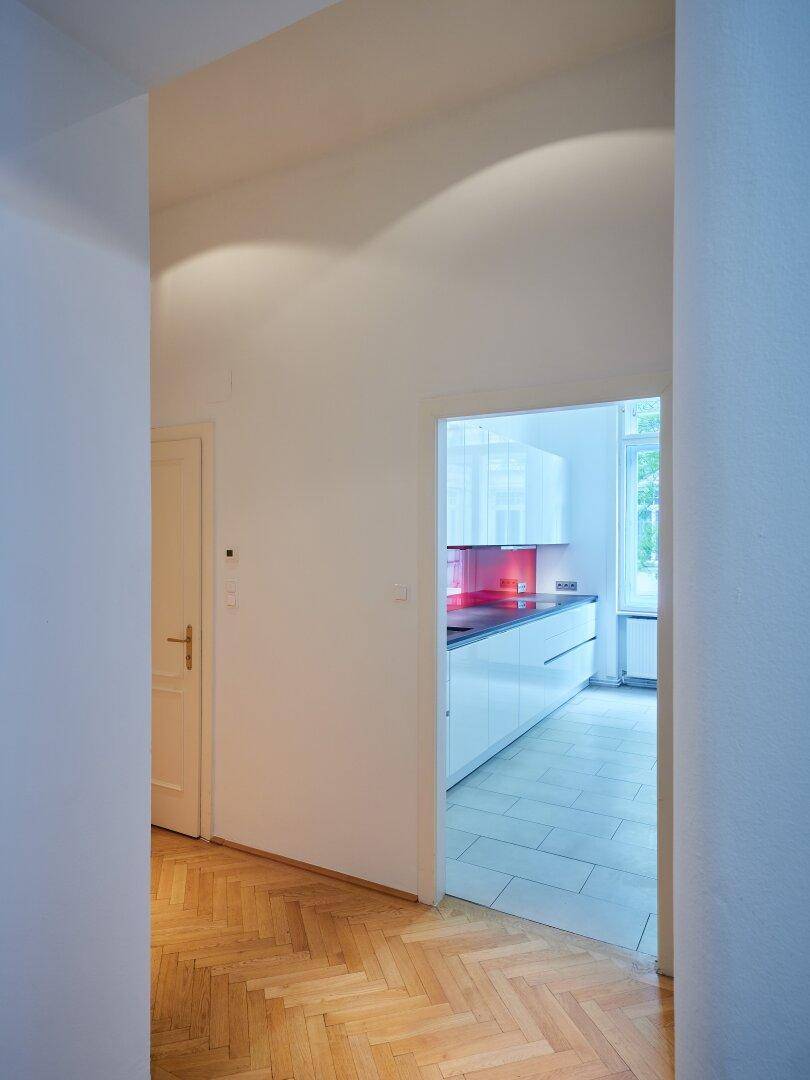Heller Flur mit Fischgrätparkettboden und Blick in die moderne Küche.