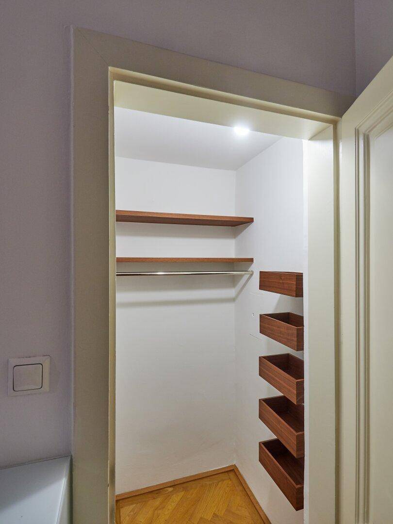 Begehbarer Kleiderschrank mit Holzregalen und Kleiderstange für Organisation.