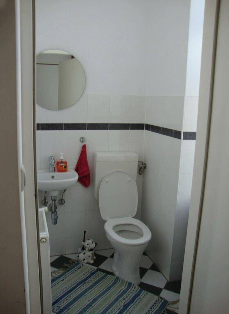 Kleines Gäste-WC mit Schachbrettmuster-Fliesenboden, Toilette und kleinem Waschbecken.