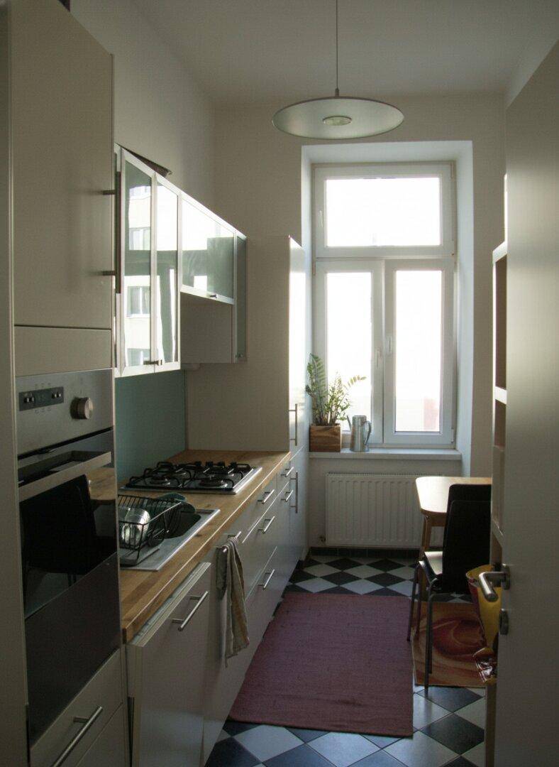 Schmale Küche mit modernen Einbauschränken, Holz-Arbeitsplatte und einem Fenster mit Blick nach draußen.