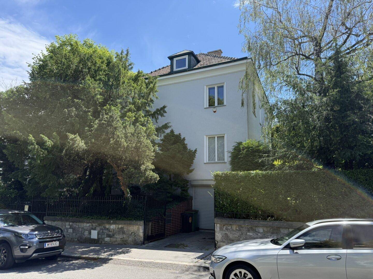 Vorderansicht eines Wohnhauses von der Straße aus, umgeben von Bäumen und einem Zaun.