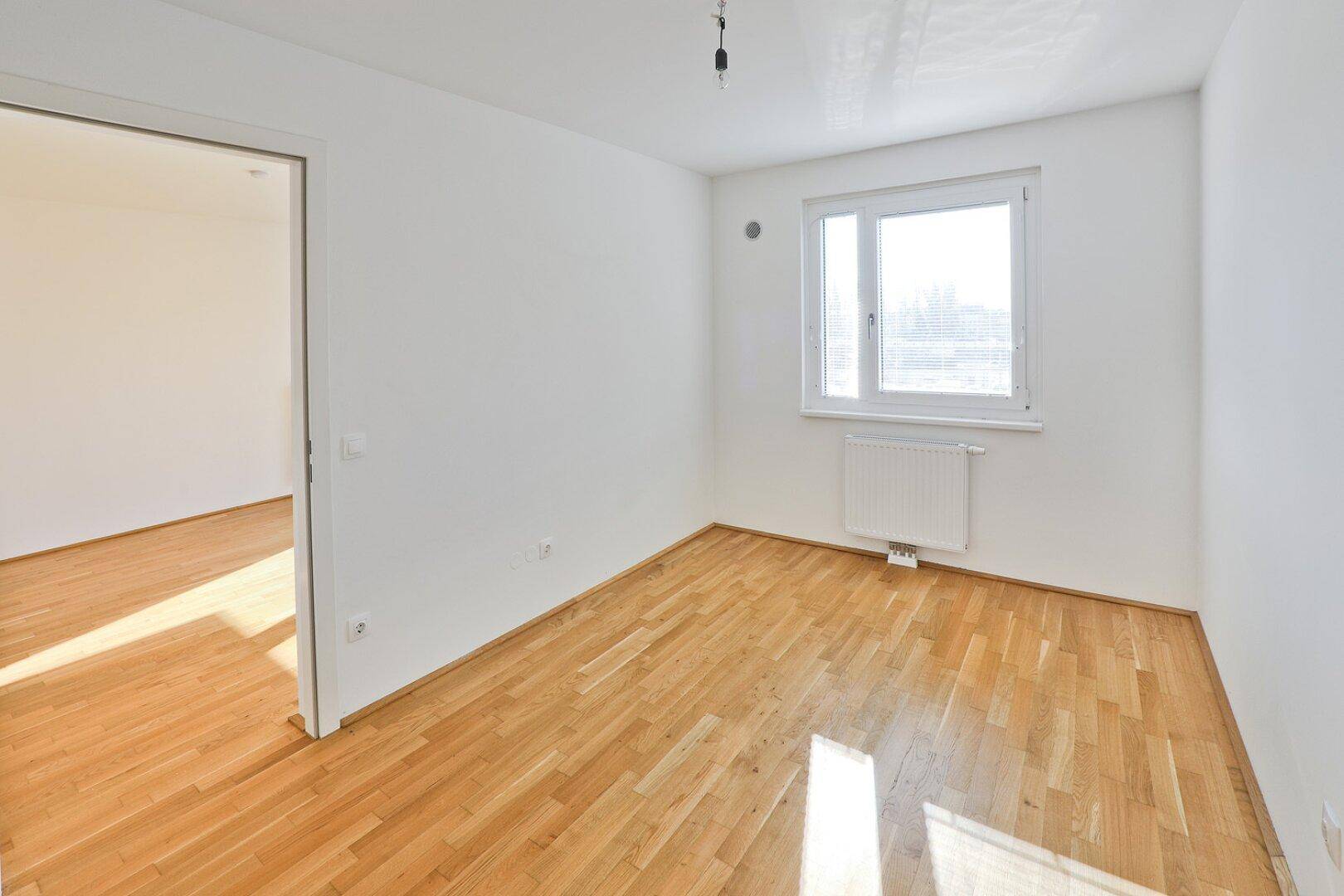 Leeres Schlafzimmer mit Parkettboden und großem Fenster für viel Tageslicht.