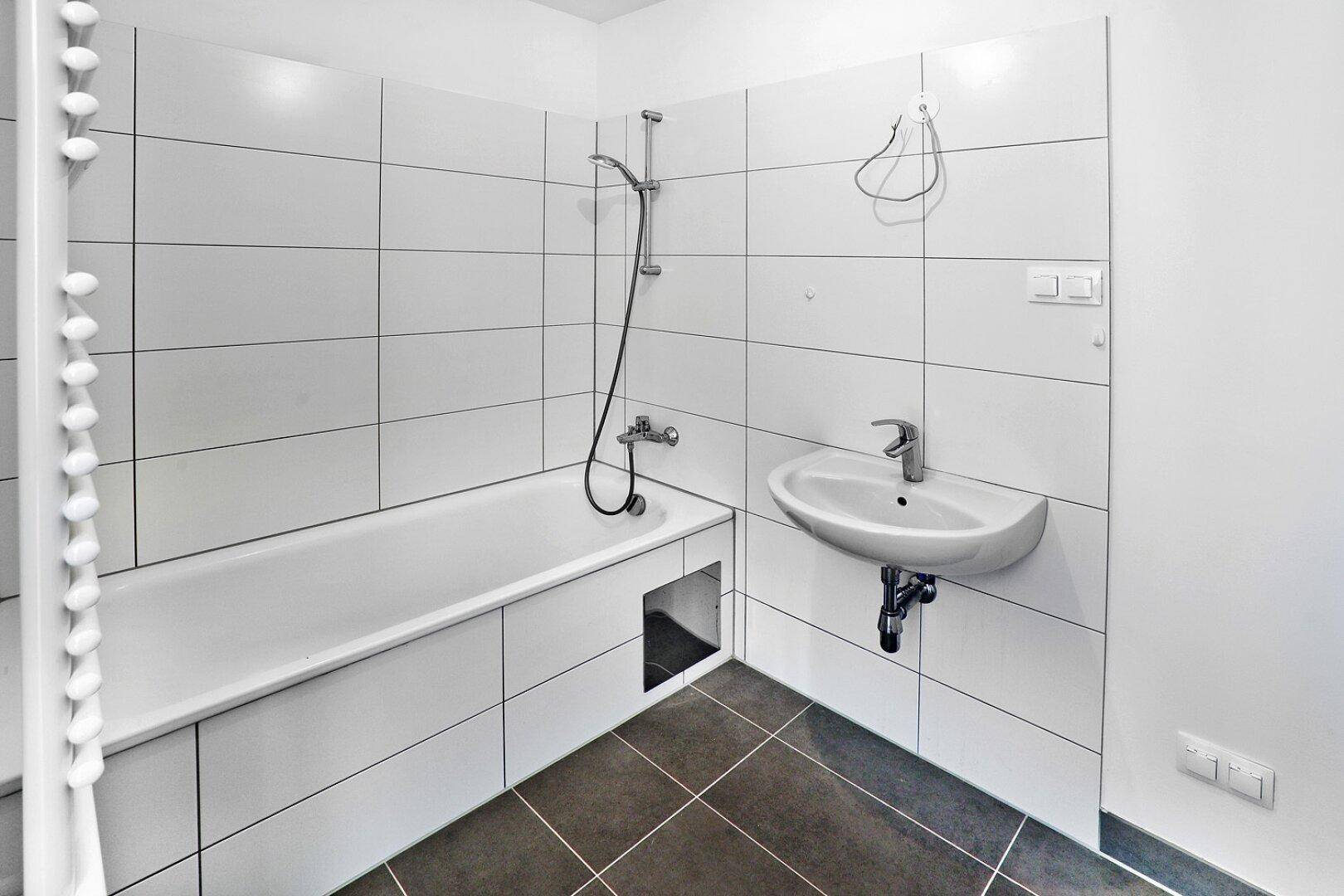 Helles Badezimmer mit Badewanne, Waschbecken und modernen Fliesen.