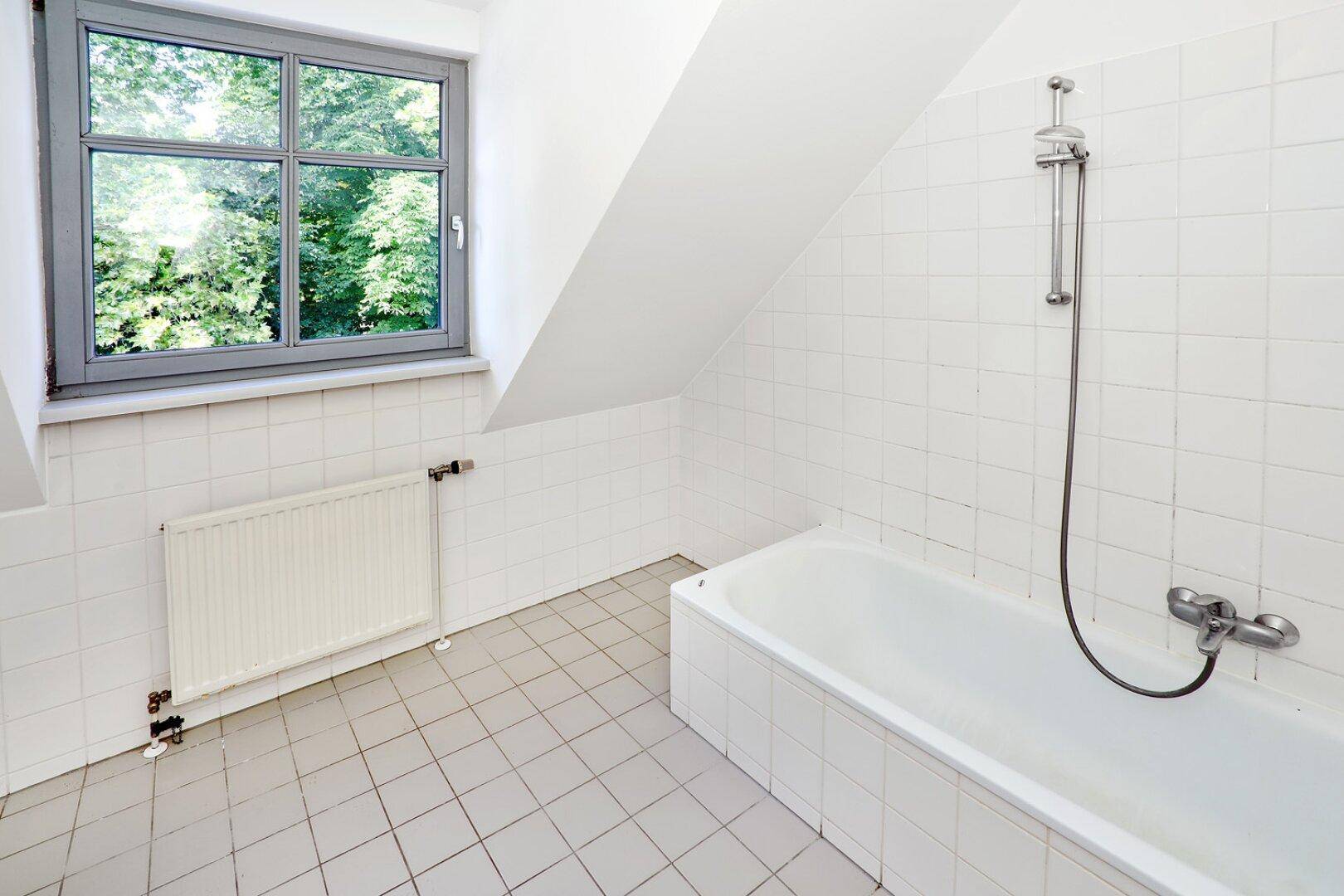 Badezimmer im Dachgeschoss mit Badewanne, Fliesen und Fenster mit Blick ins Grüne.