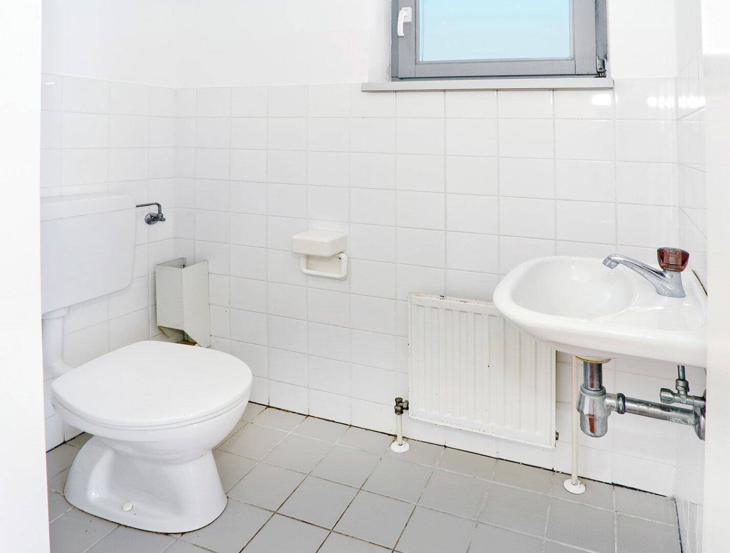 Kleines WC mit Waschbecken, Toilette und Fenster, hell gefliest.