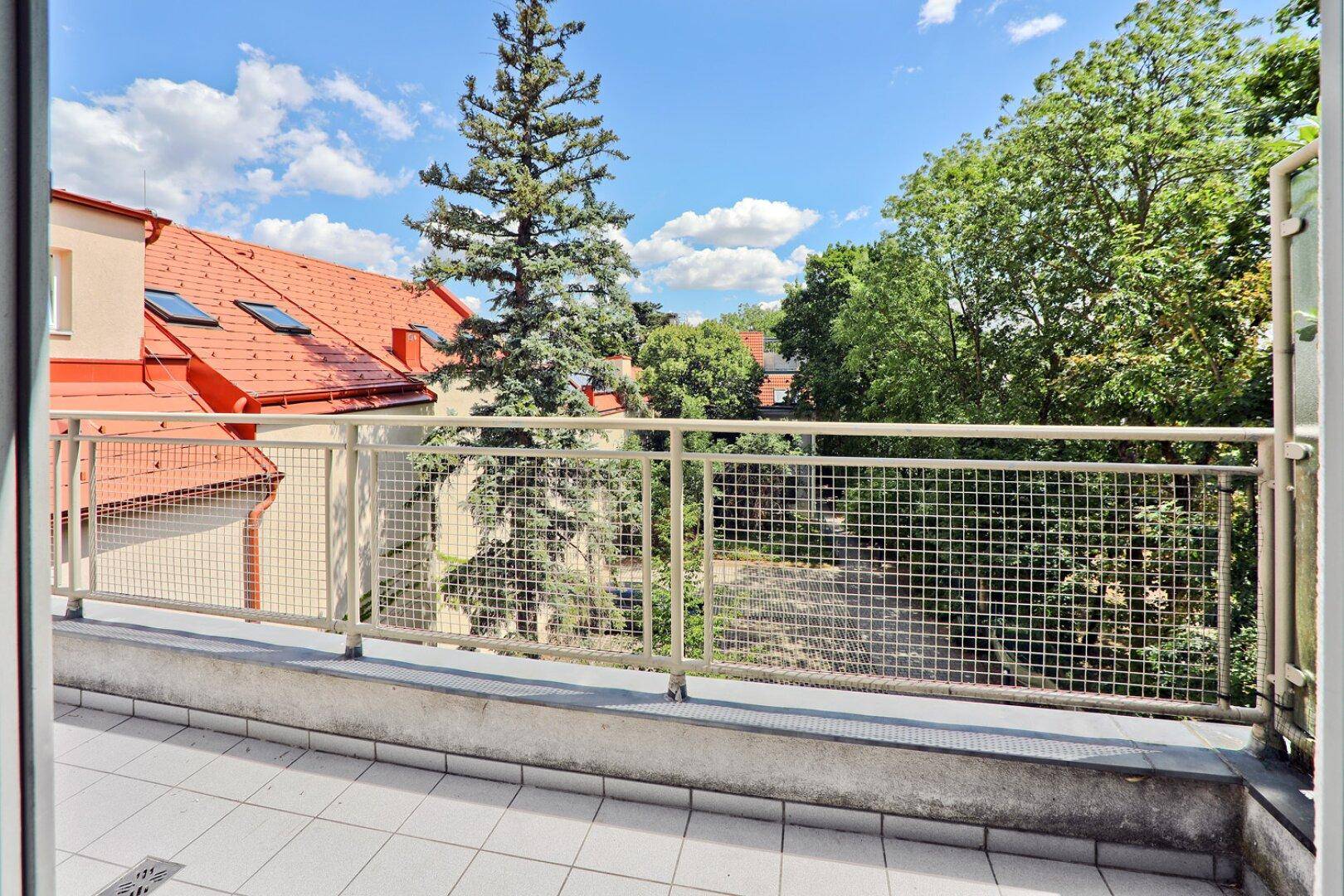 Balkon mit Gittergeländer und weitem Blick auf grüne Bäume und Dächer.