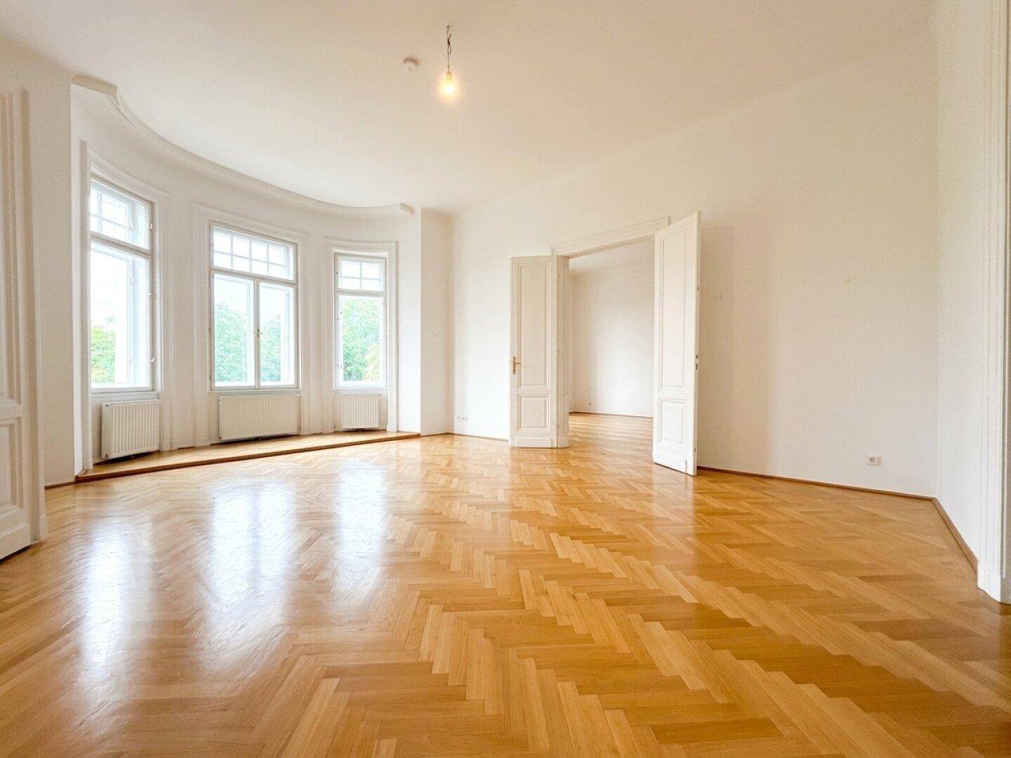 Geräumiges Zimmer mit glänzendem Fischgrätparkett und einem schönen Erker mit großen Fenstern.