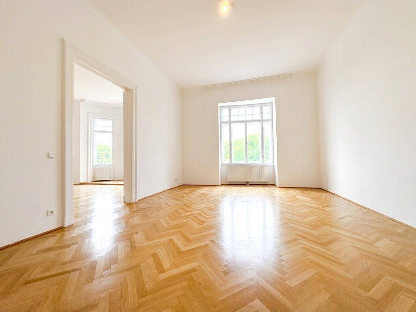 Helles Zimmer mit klassischem Fischgrätparkett und einem großen Fenster, das viel Licht hereinlässt.