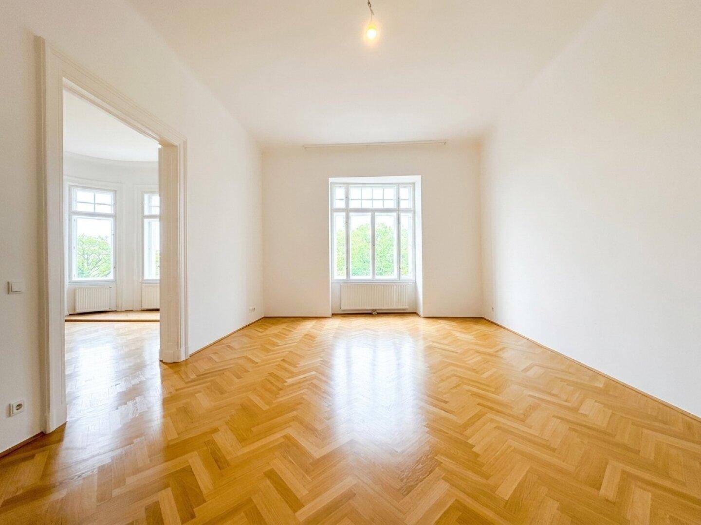 Lichtdurchflutetes Zimmer mit elegantem Fischgrätparkett und einem großen Fenster, ideal für individuelle Gestaltung.