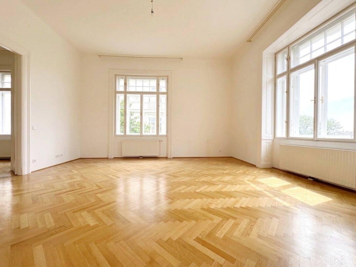 Großes, helles Zimmer mit Fischgrätparkett und zwei hohen Fenstern, die eine angenehme Atmosphäre schaffen.