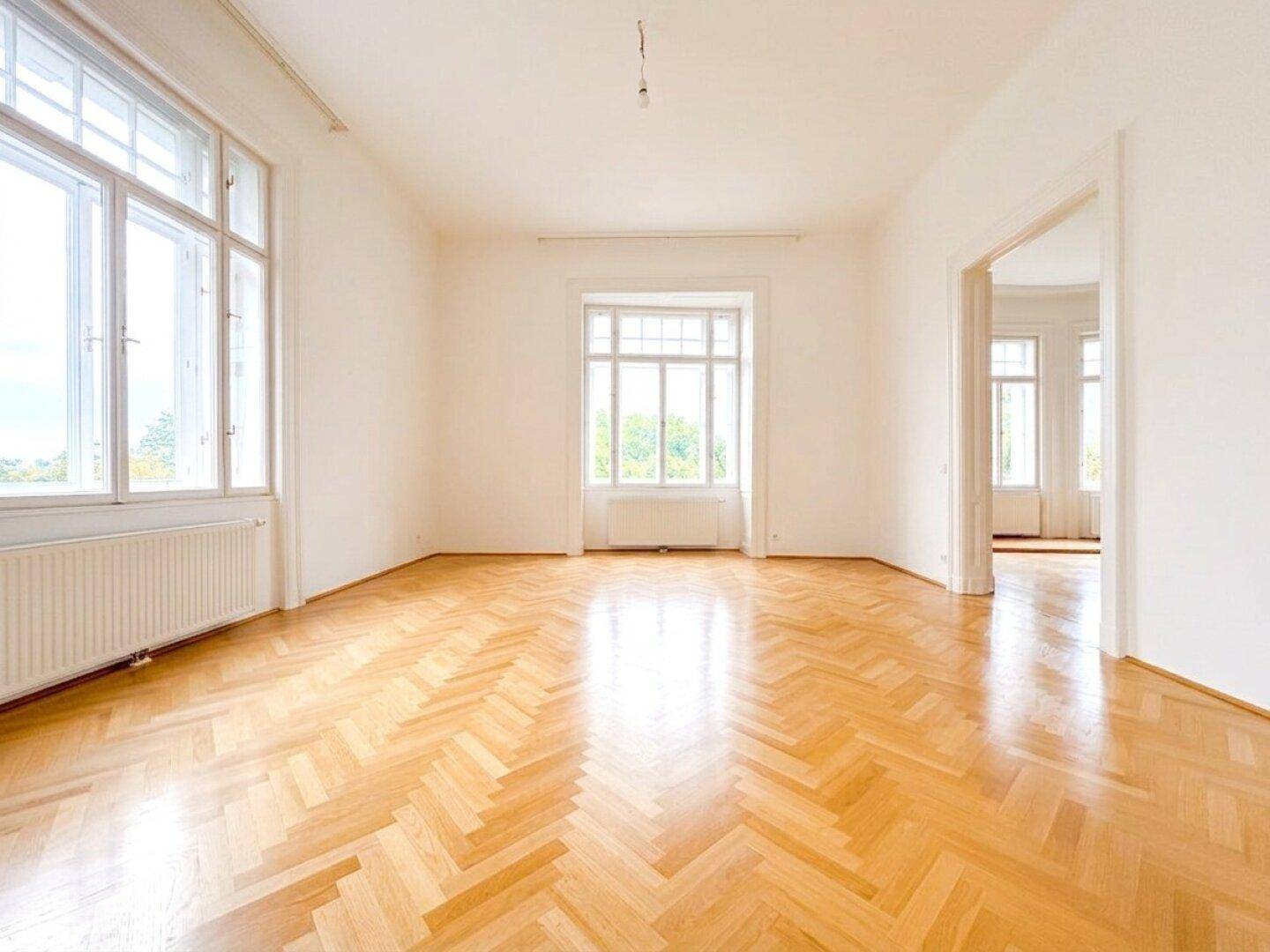 Geräumiges Zimmer mit glänzendem Fischgrätparkett und hohen Fenstern, das viel Tageslicht bietet.