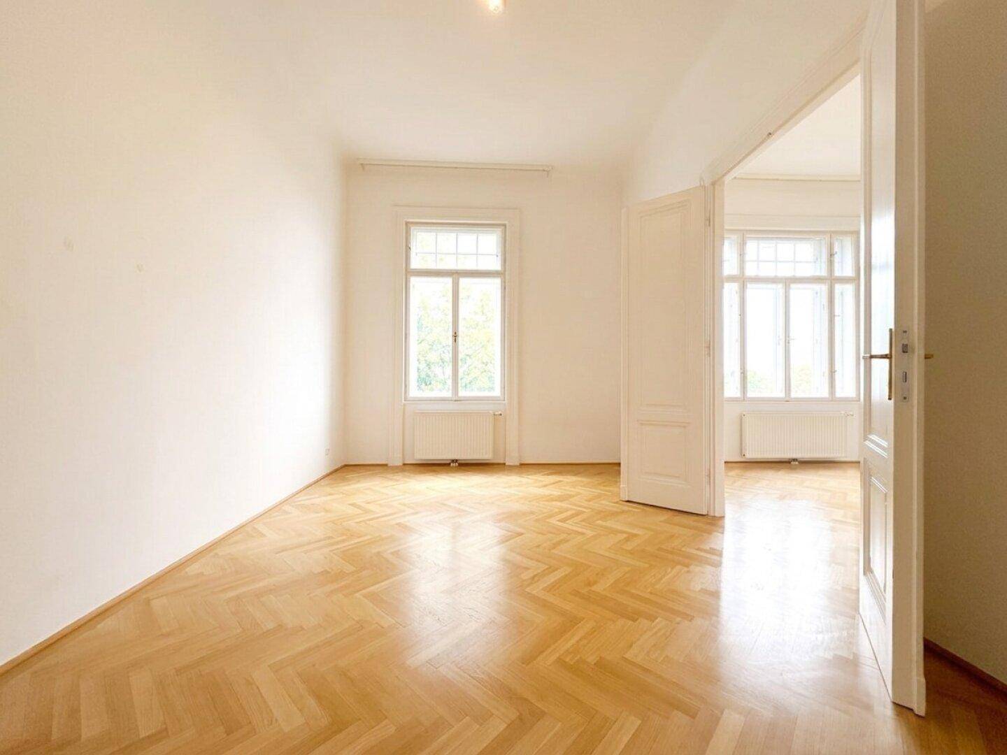 Lichtdurchflutetes Zimmer mit elegantem Fischgrätparkett und einem großen Fenster, das vielseitig nutzbar ist.