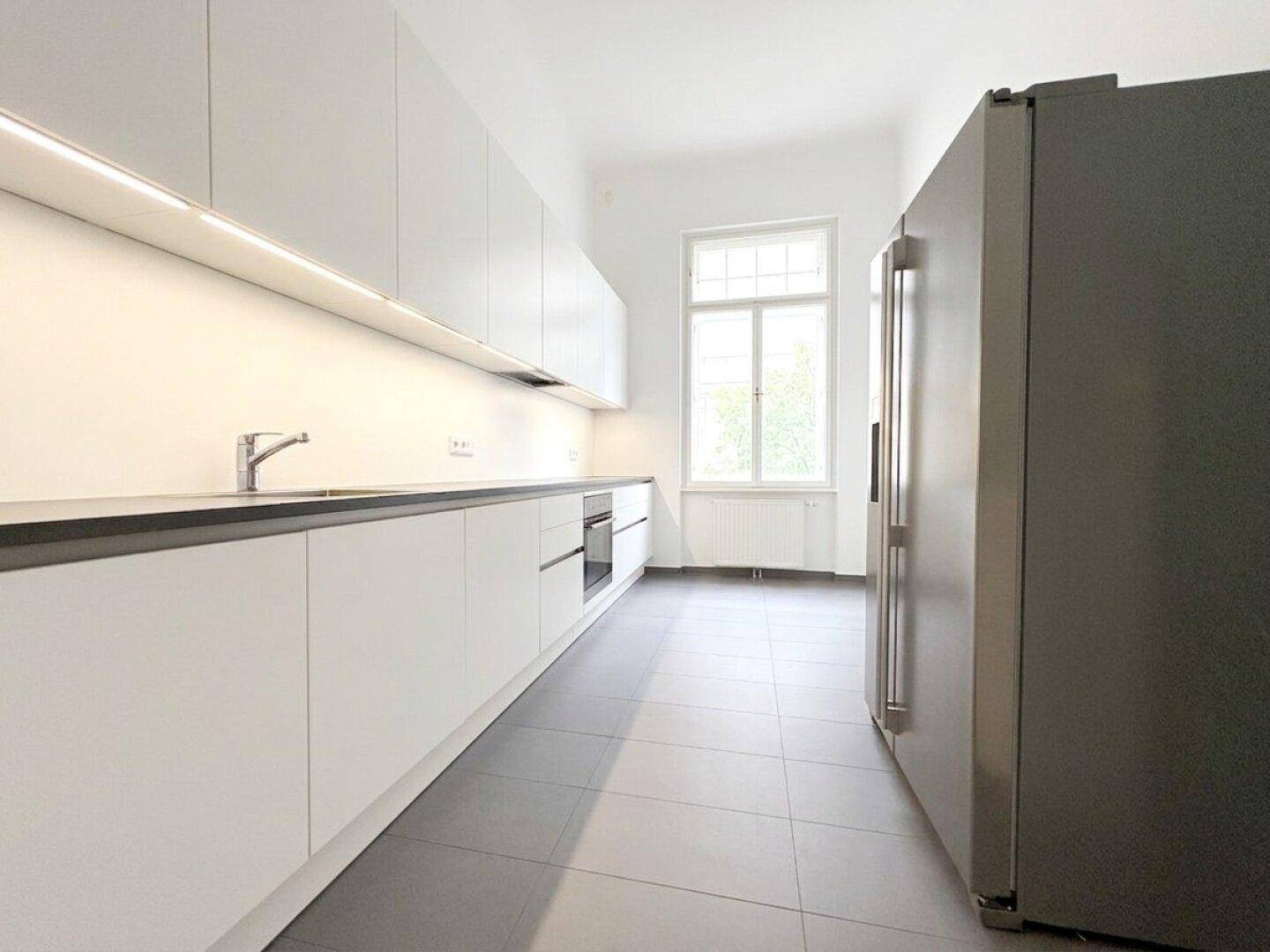 Moderne, helle Küche mit weißen Schränken, dunkler Arbeitsplatte und einem großen Kühlschrank.