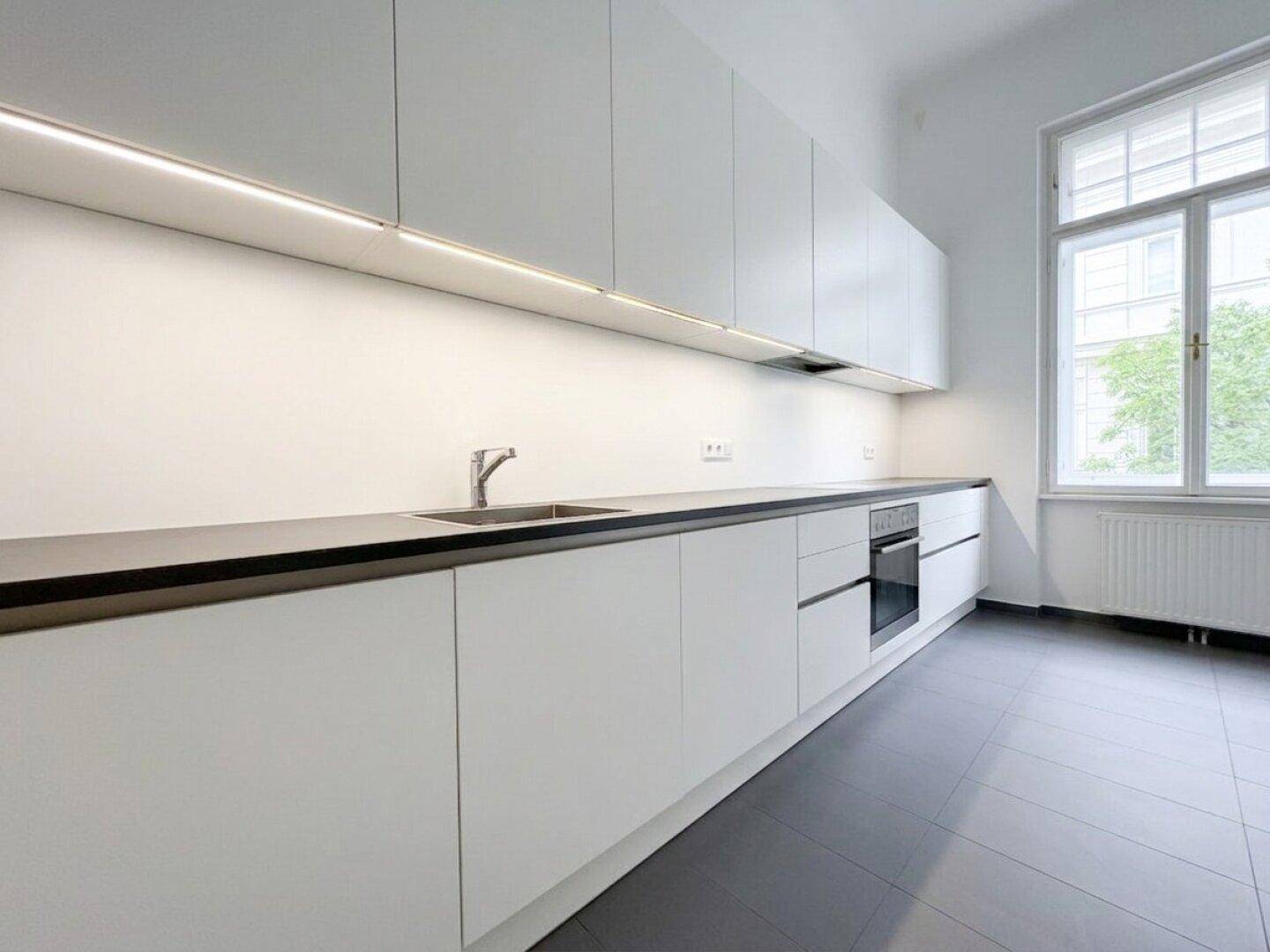 Helle, moderne Küche mit weißen Schränken, dunkler Arbeitsplatte und integriertem Backofen.