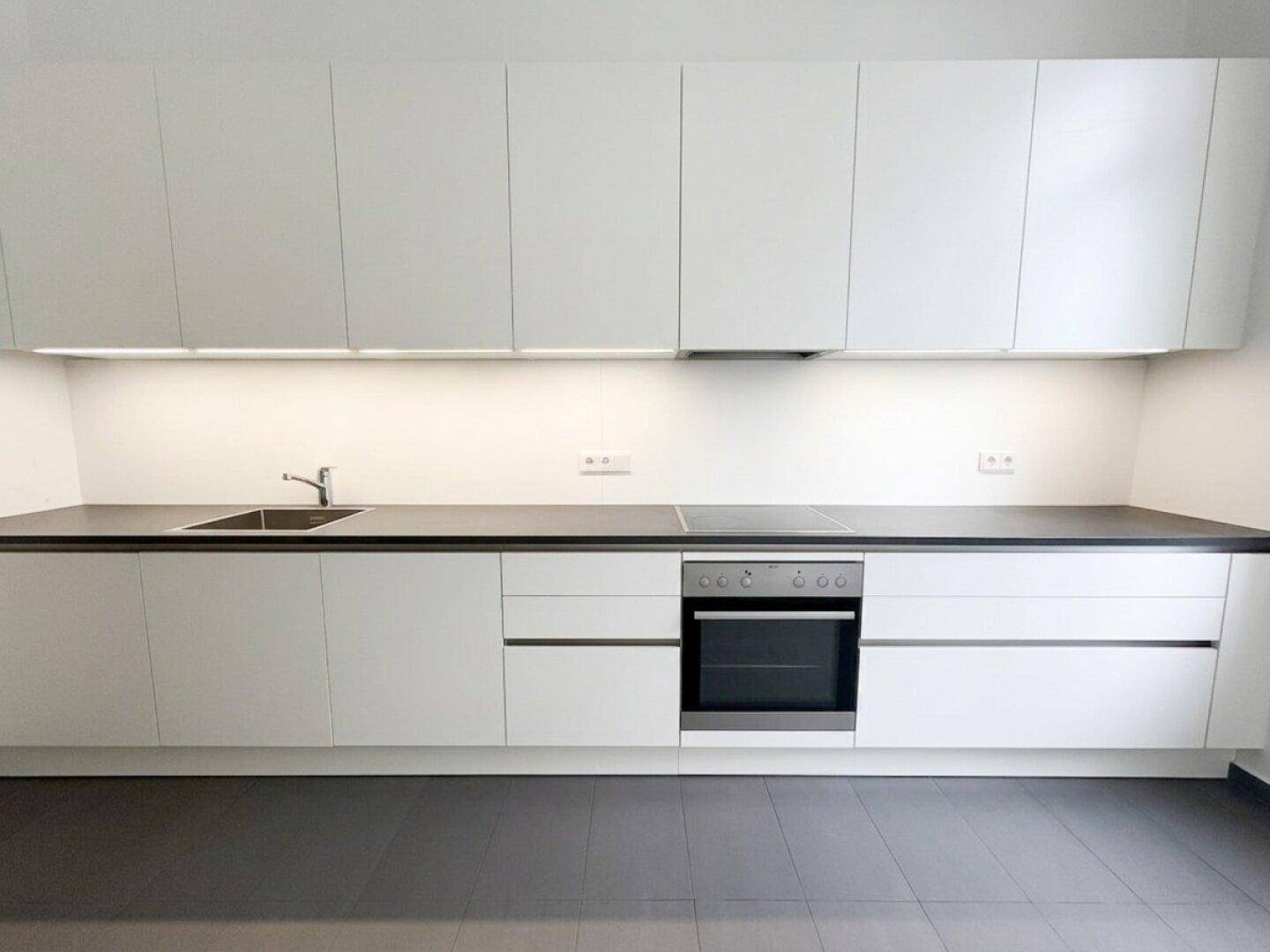 Moderne, helle Küche mit weißen Schränken, dunkler Arbeitsplatte und integriertem Kochfeld und Backofen.