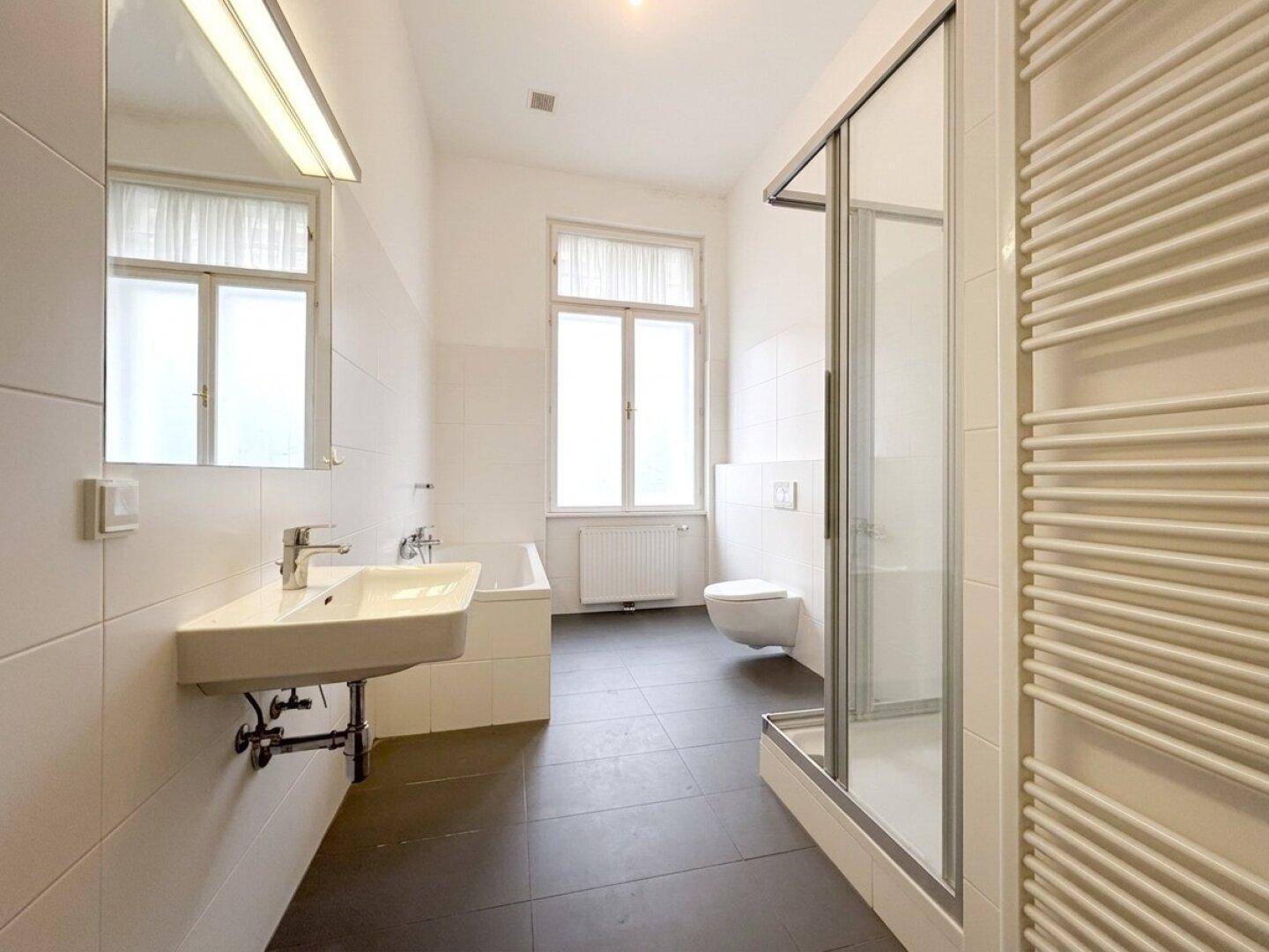 Helles Badezimmer mit Badewanne, Duschkabine, WC und beheiztem Handtuchhalter.