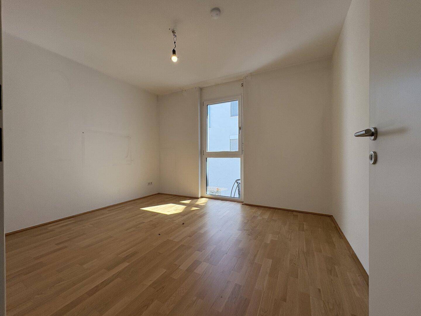 Geräumiges Schlafzimmer mit Holzboden und Fenster, das Sonnenlicht in den Raum bringt.