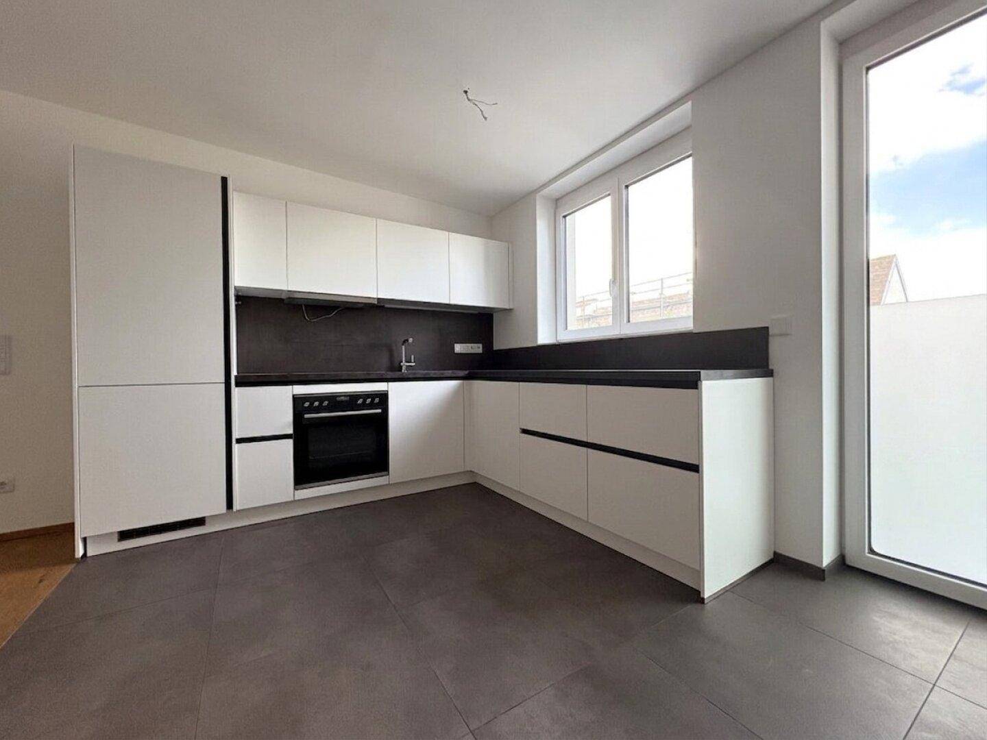 Moderne Einbauküche in Weiß mit dunkler Arbeitsplatte und Fenster für Tageslicht.