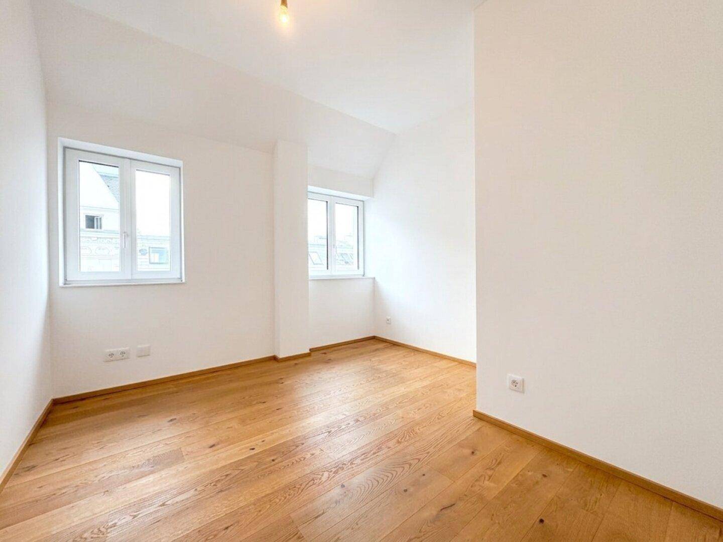 Unmöbliertes Zimmer mit Eichenparkett und großen Fenstern, ideal als Schlaf- oder Arbeitszimmer.