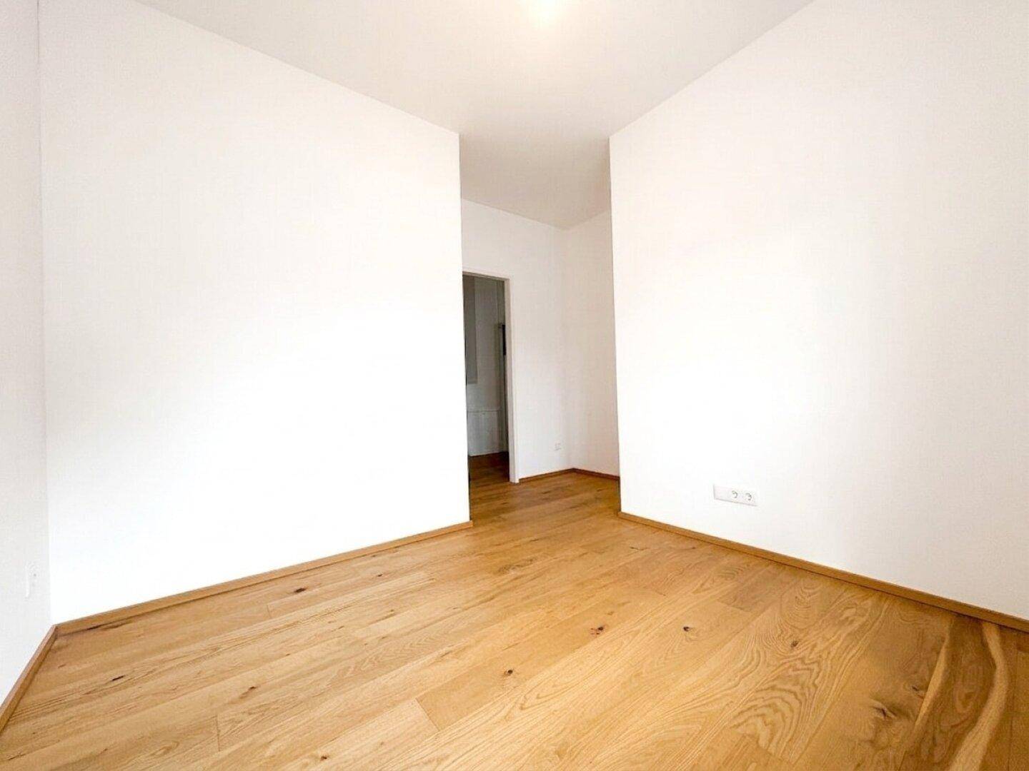 Helles Zimmer mit Holzboden und weiß gestrichenen Wänden, bereit zur individuellen Gestaltung.
