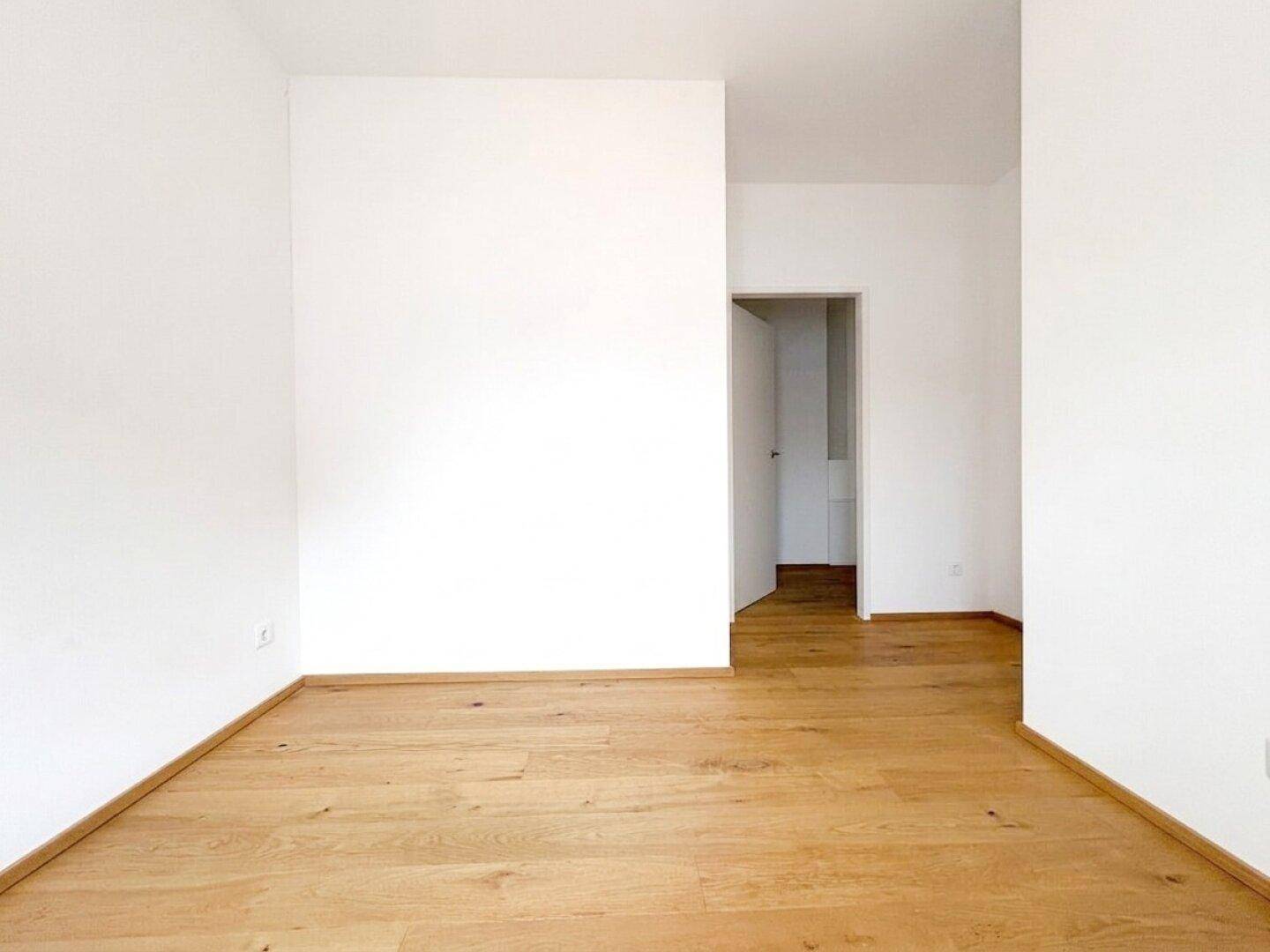 Leeres Zimmer mit Parkettboden und Zugang zu einem weiteren Raum, ideal für flexible Nutzung.