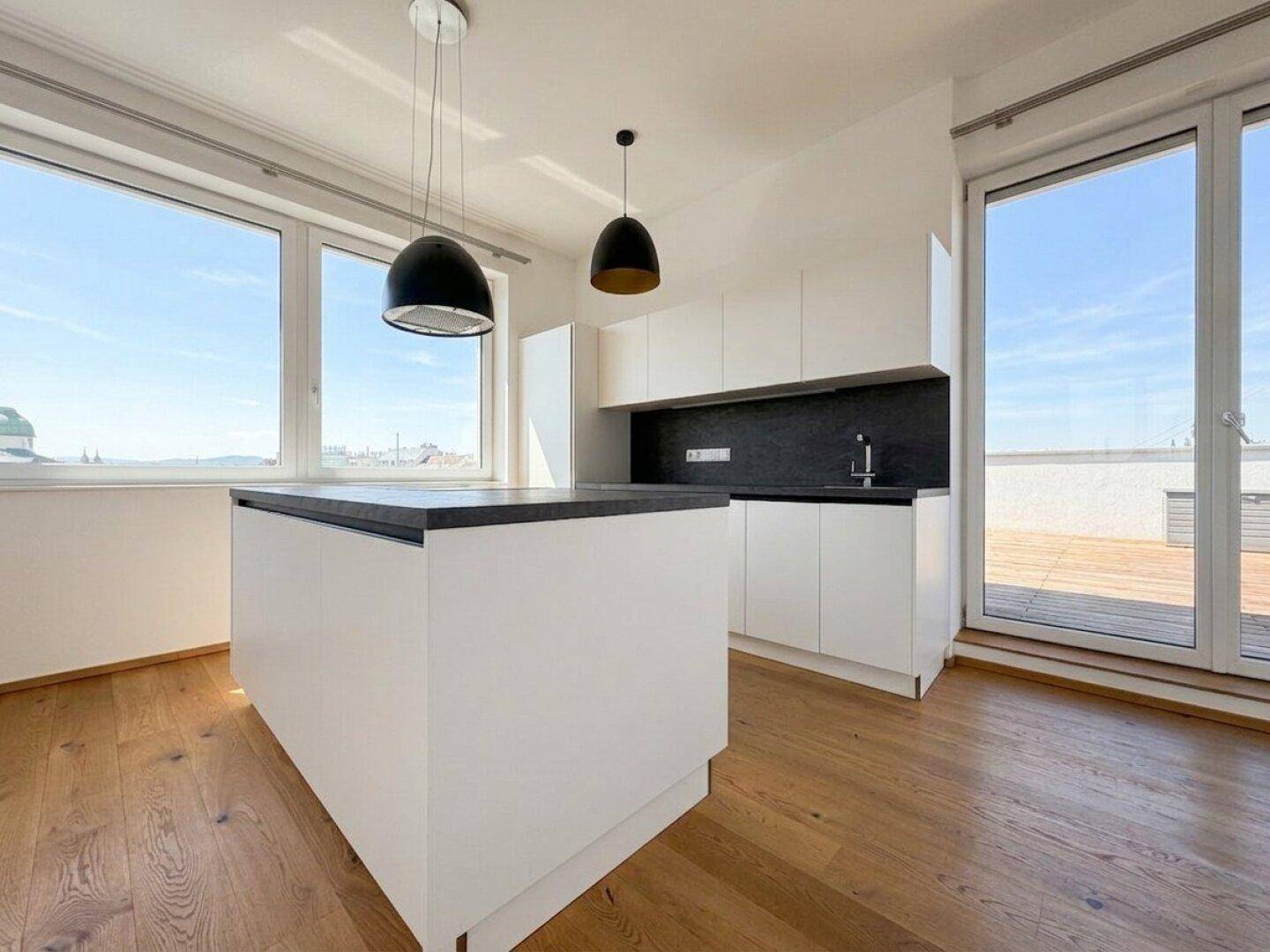 Moderne Küche mit Kücheninsel, dunkler Arbeitsplatte und direktem Zugang zur sonnigen Dachterrasse.