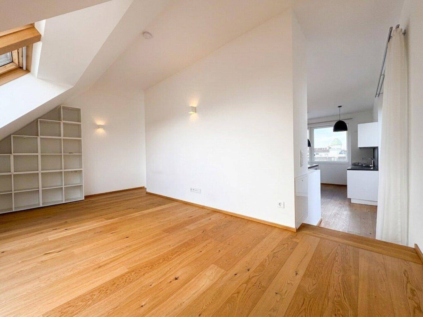 Heller Wohnbereich im Dachgeschoss mit Holzboden, Dachfenstern und integriertem Regal.