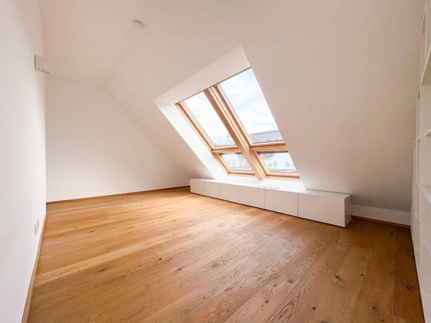 Geräumiger Dachgeschossraum mit Holzboden und großen Dachfenstern für viel Tageslicht.