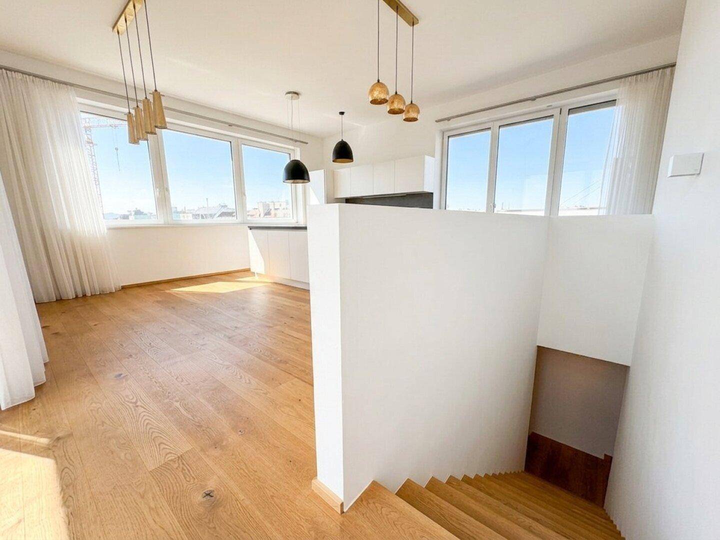 Offener Wohnbereich mit Holzboden, moderner Küche und Treppe zum unteren Geschoss.