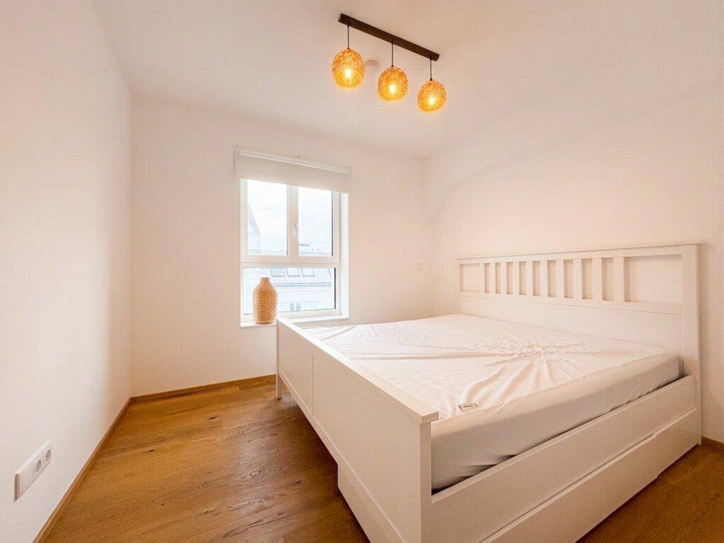 Gemütliches Schlafzimmer mit Holzboden, weißem Bett und dekorativer Beleuchtung.