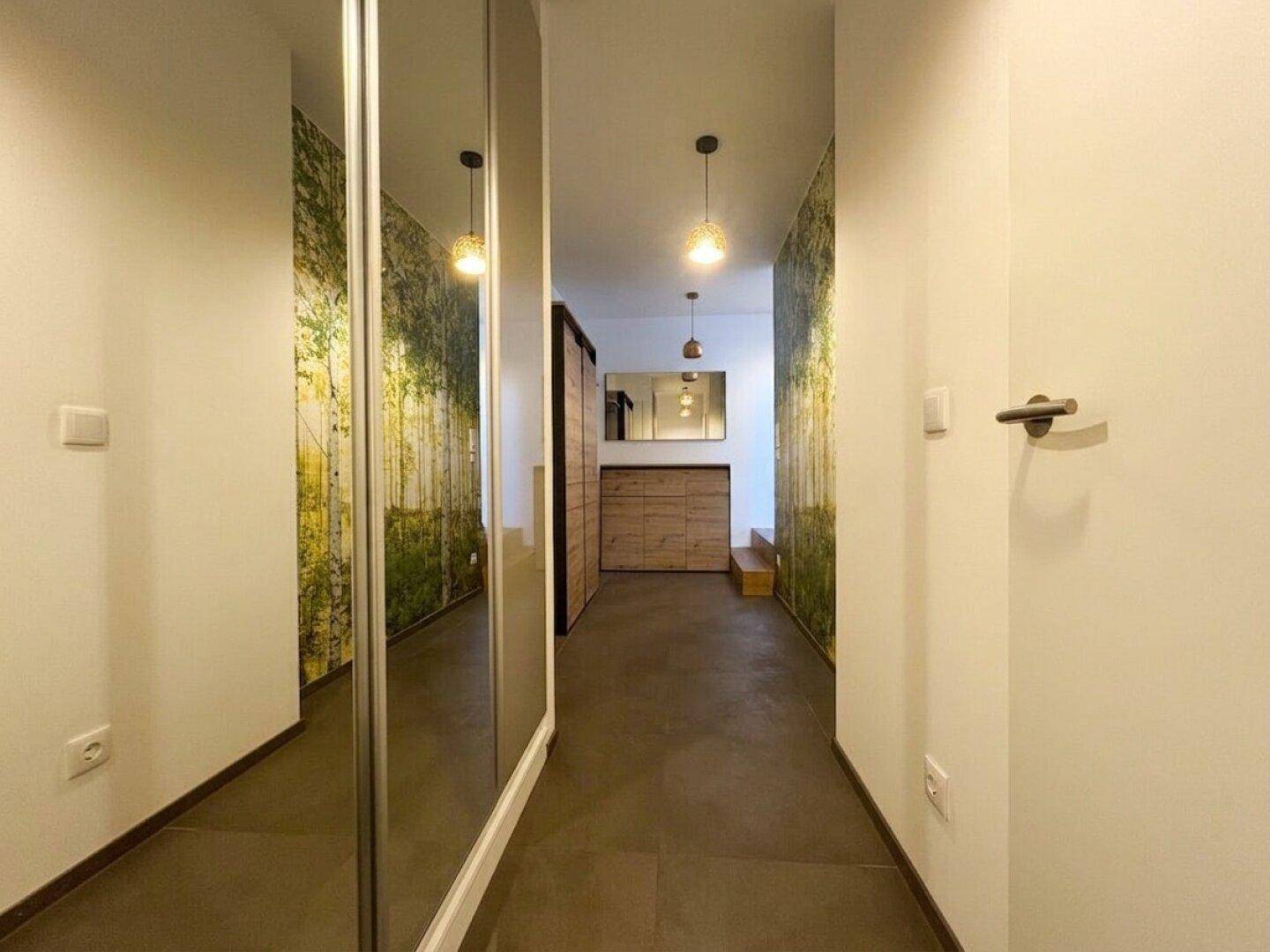 Langer Flur mit Spiegeln, Waldtapete und Fliesenboden, der zu weiteren Räumen führt.