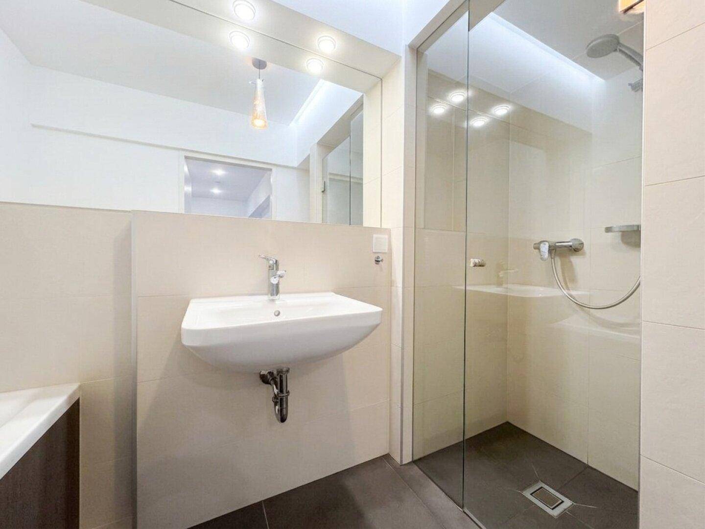 Helles Badezimmer mit modernem Waschbecken, großer Dusche und Fliesenboden.