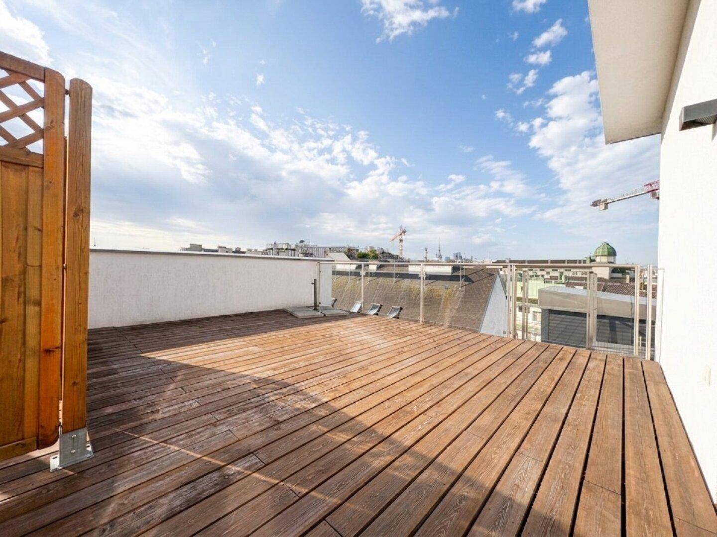 Sonniger Außenbereich auf der Dachterrasse mit Holzdielen und Panoramablick.