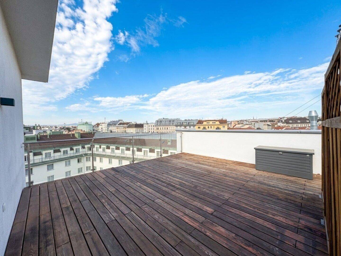 Geräumige Dachterrasse mit Holzboden und weitem Blick über die Stadt.