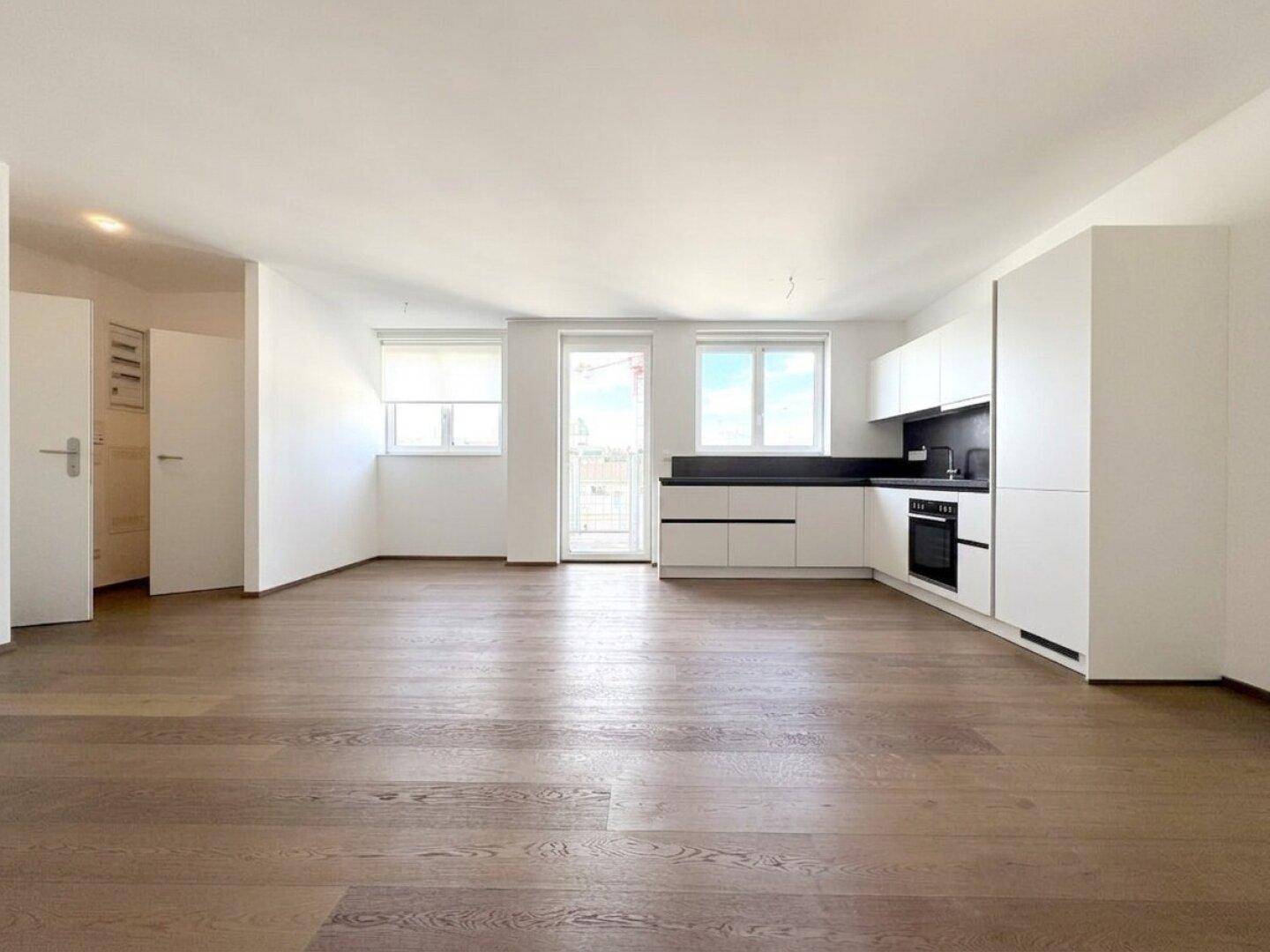 Geräumiger Wohn- und Essbereich mit offener Küche und Zugang zu einem Balkon, ausgestattet mit hochwertigem Holzboden.